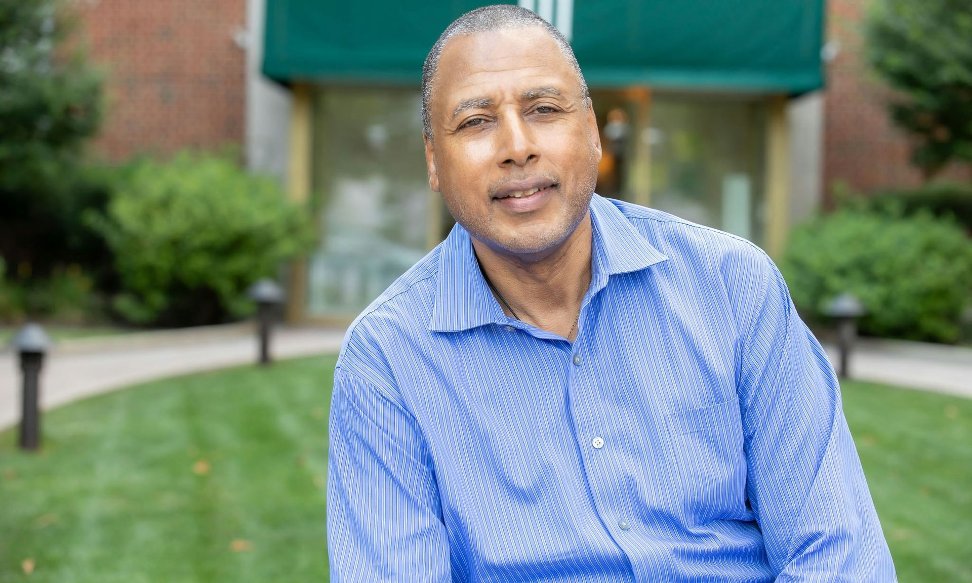 Man in blue shirt smiles outside a building with green awning.